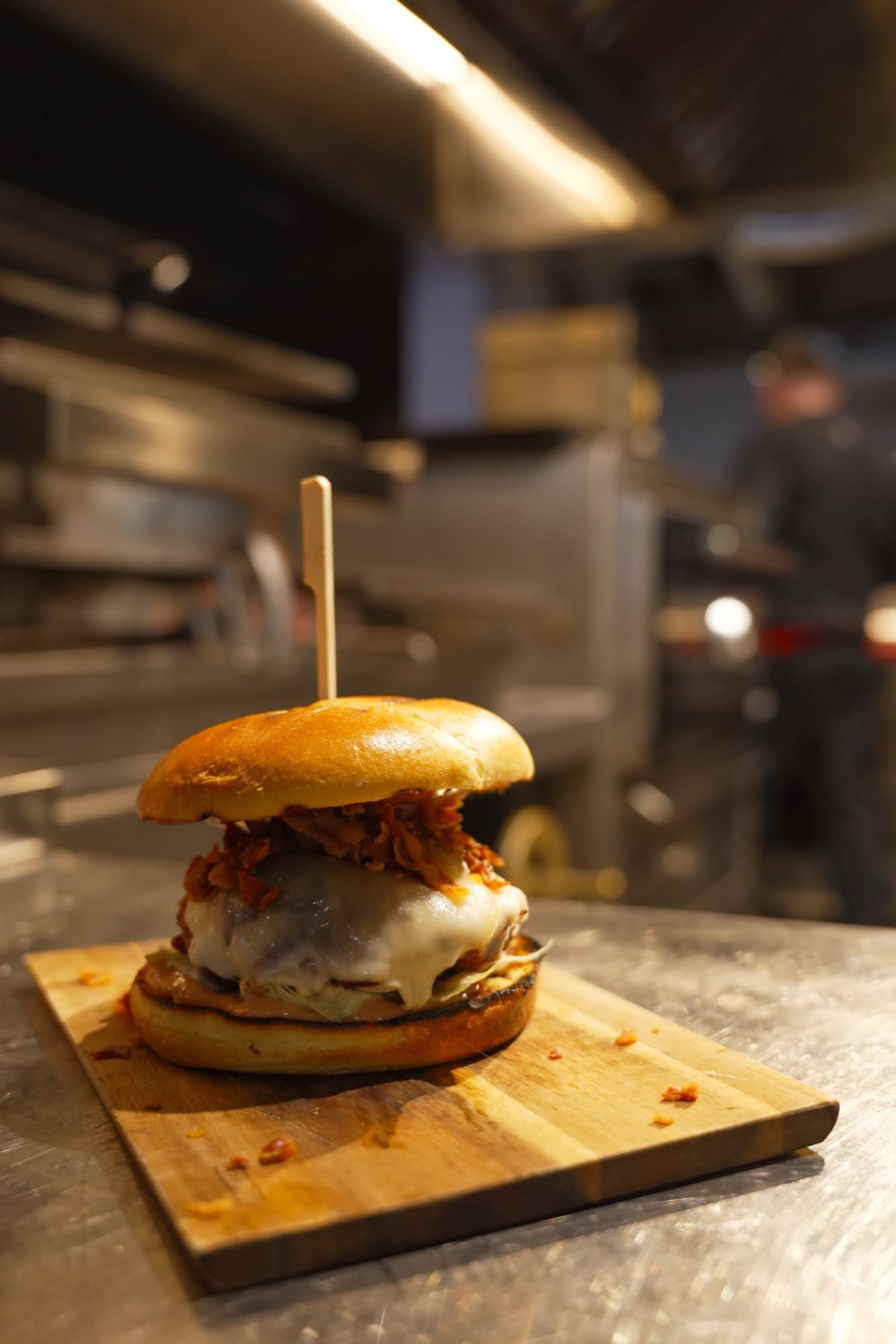 Charcoal-grilled burger on wooden board with chef in background
