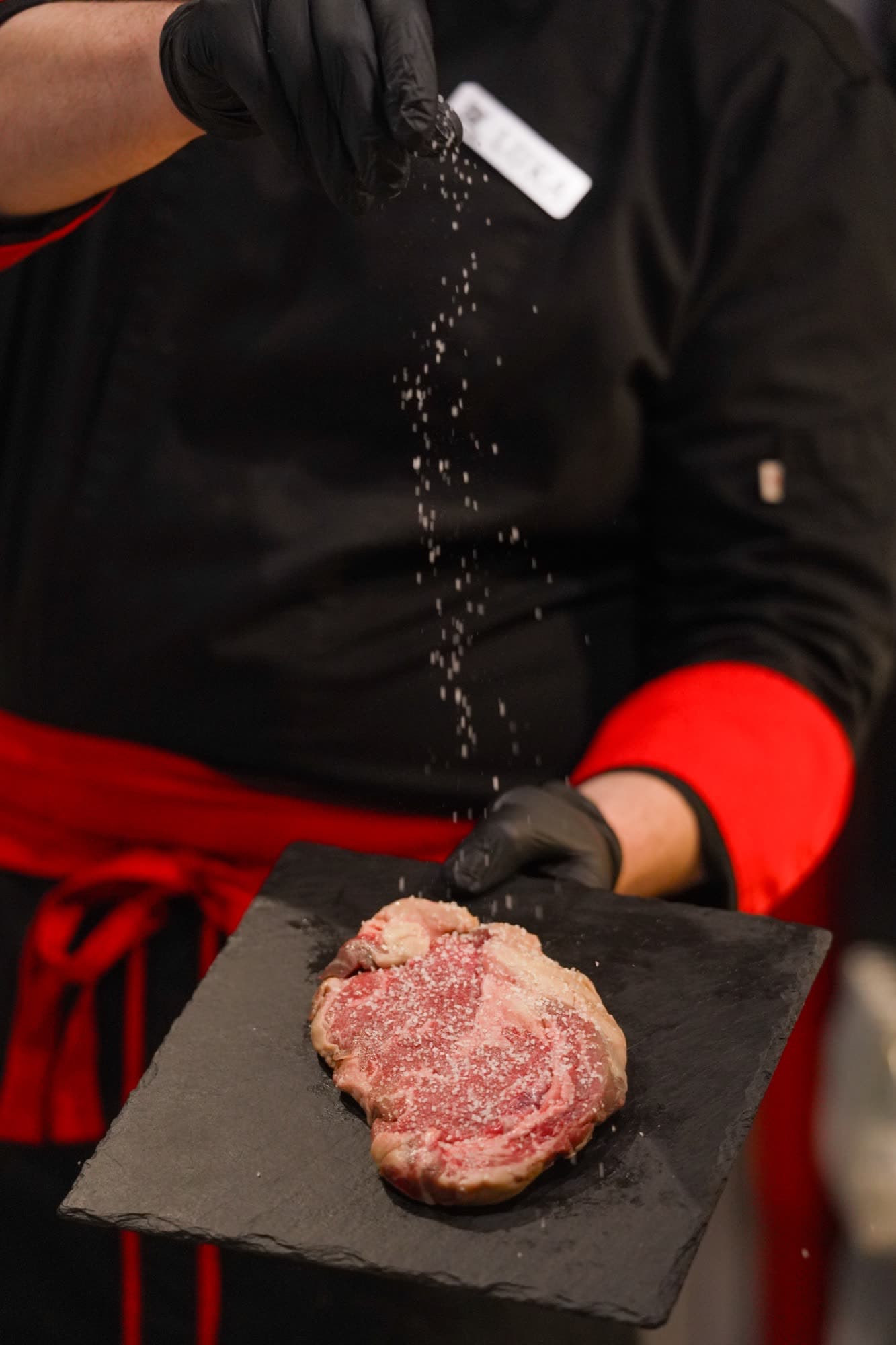 Chef seasoning rib eye with salt falling onto the meat