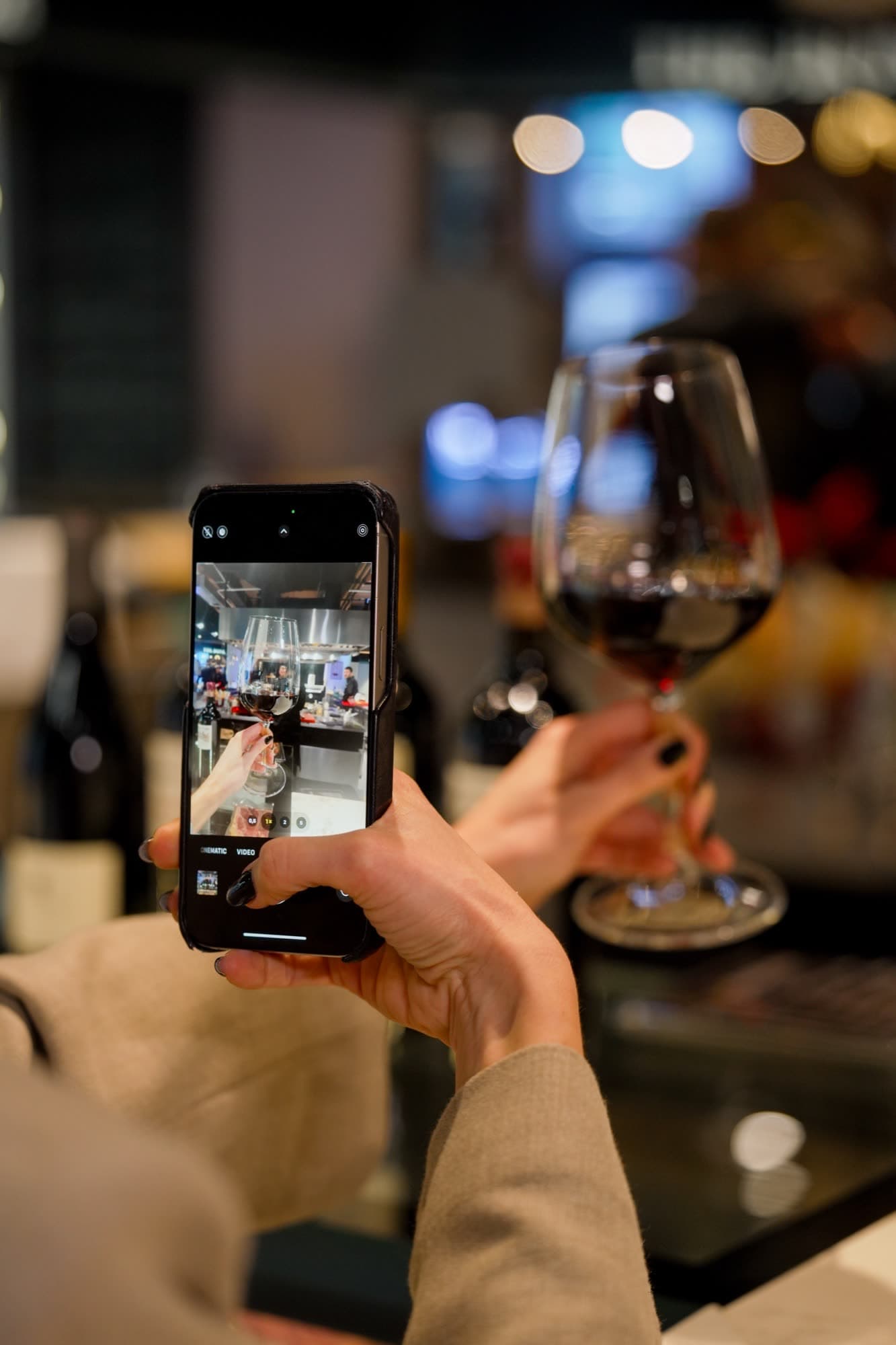 Guest photographing wine glass with phone in warm ambient lighting