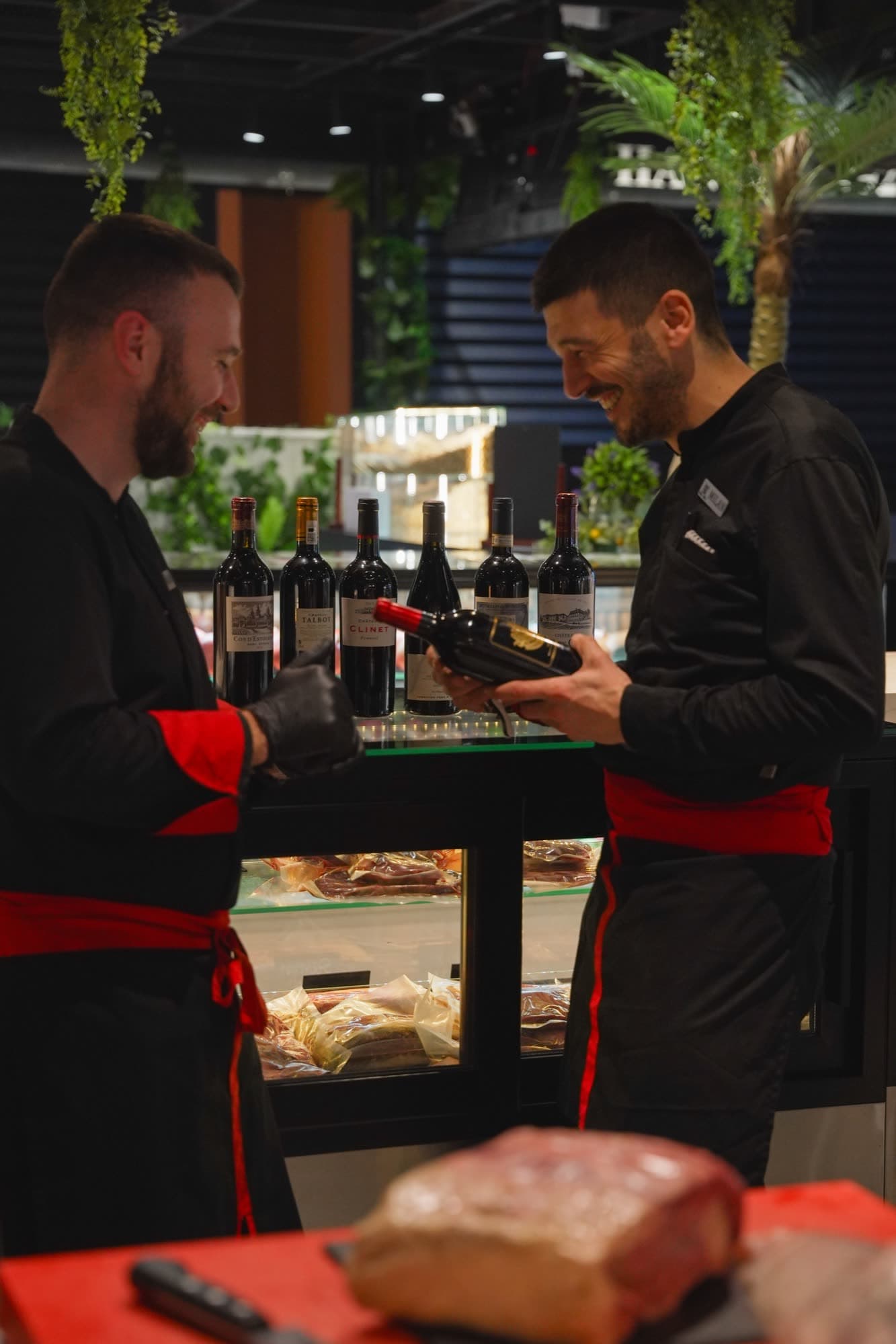 Two chefs examining wine bottles at the vitrine beside the meat display